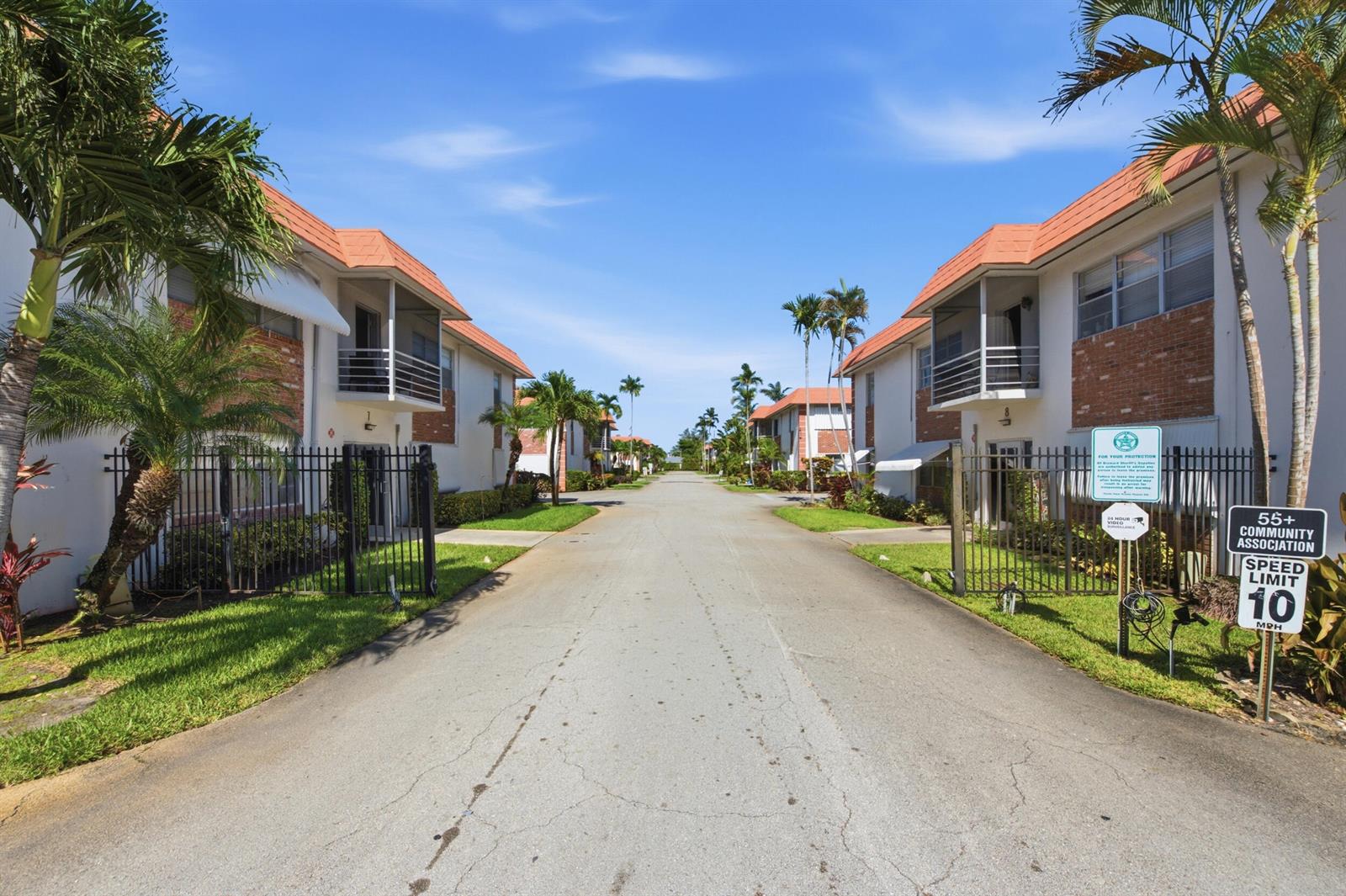 A paved road leads between two rows of two-story apartment buildings with palm trees — 3550 NW 8th Avenue # 812, Pompano Beach FL 33064, POMPANO BEACH, FL