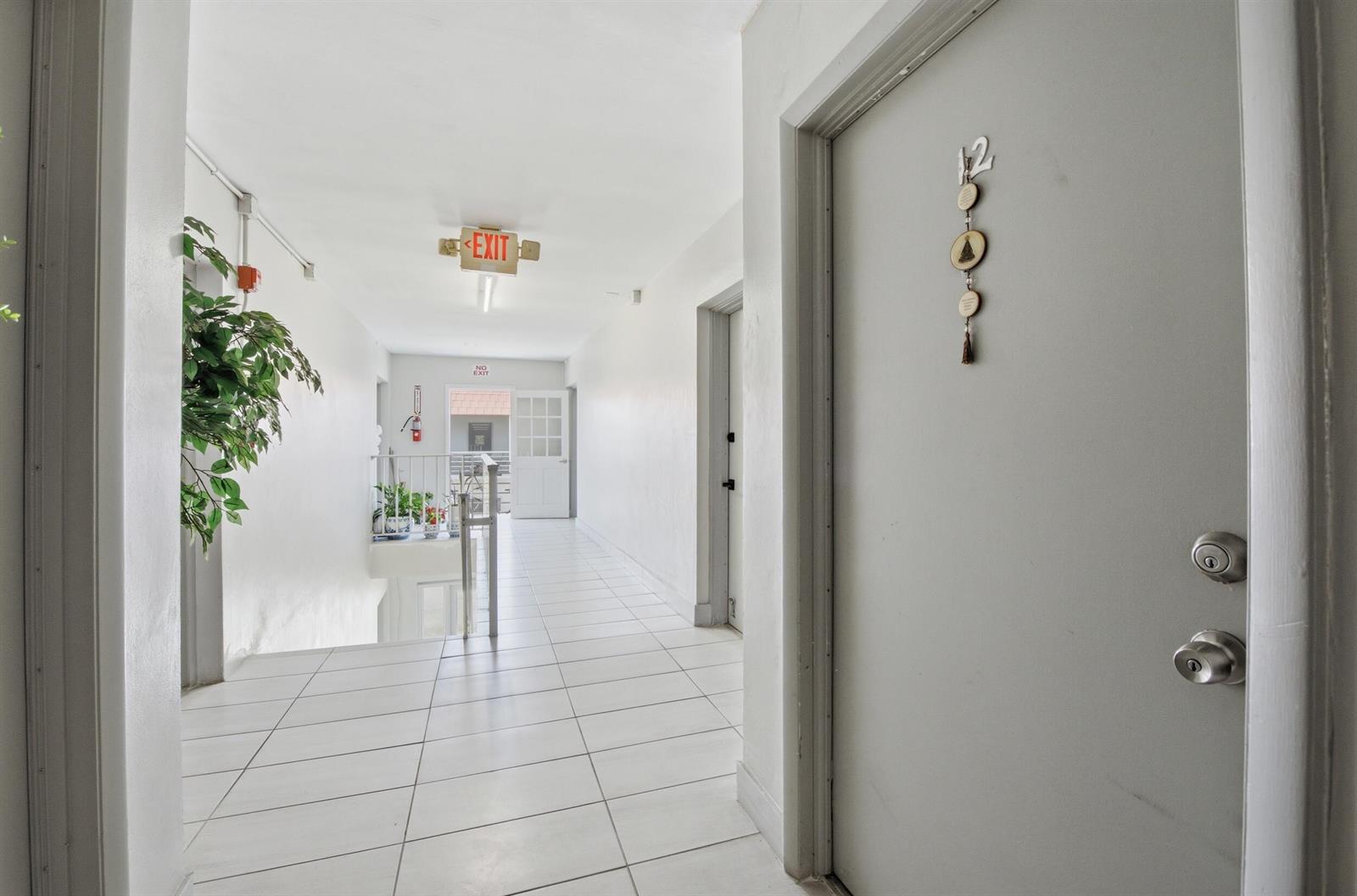 A hallway with white tile floors, a gray door labeled 12, and an exit sign — 3550 NW 8th Avenue # 812, Pompano Beach FL 33064, POMPANO BEACH, FL