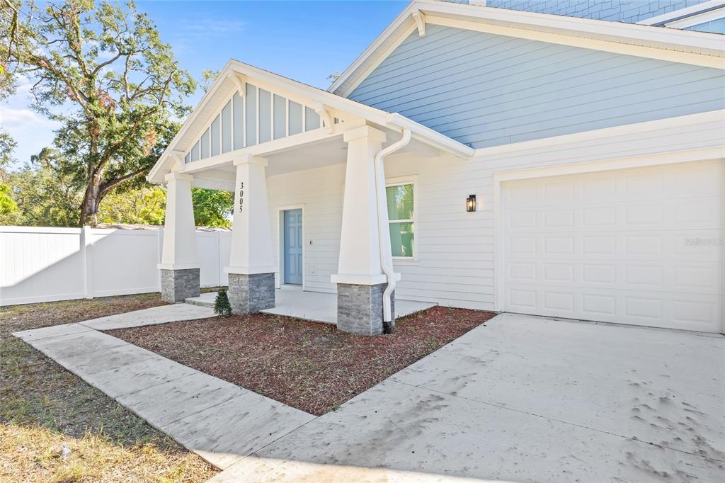 A white house exterior features a covered porch with stone-based columns and a blue door — 3005 E 17TH AVENUE, TAMPA, FL