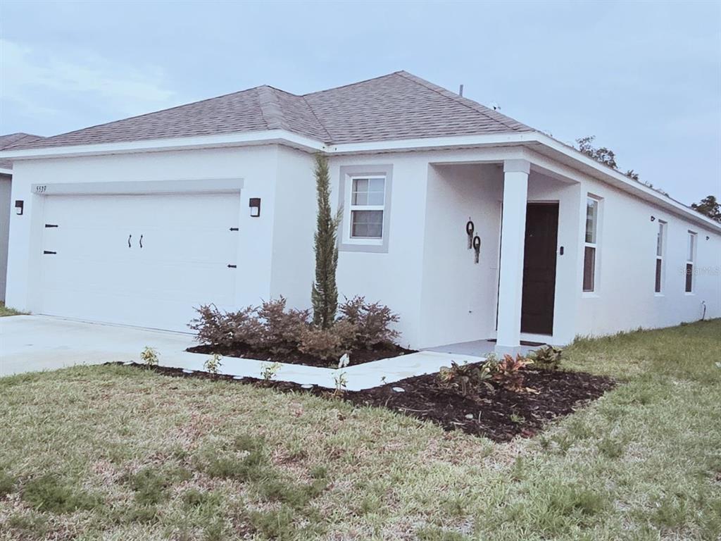 A single-story white stucco house features a two-car garage and a covered front entryway — 5539 MADDIE DRIVE, HAINES CITY, FL
