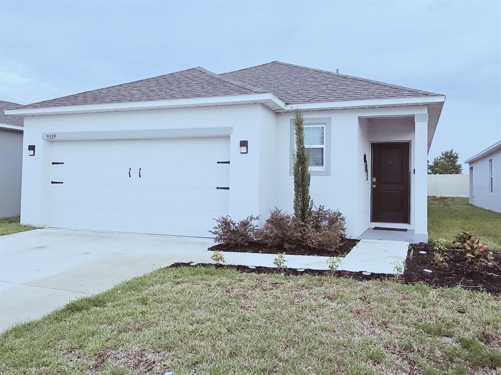 A single-story house with a white stucco exterior, a two-car garage, and a dark door — 5539 MADDIE DRIVE, HAINES CITY, FL