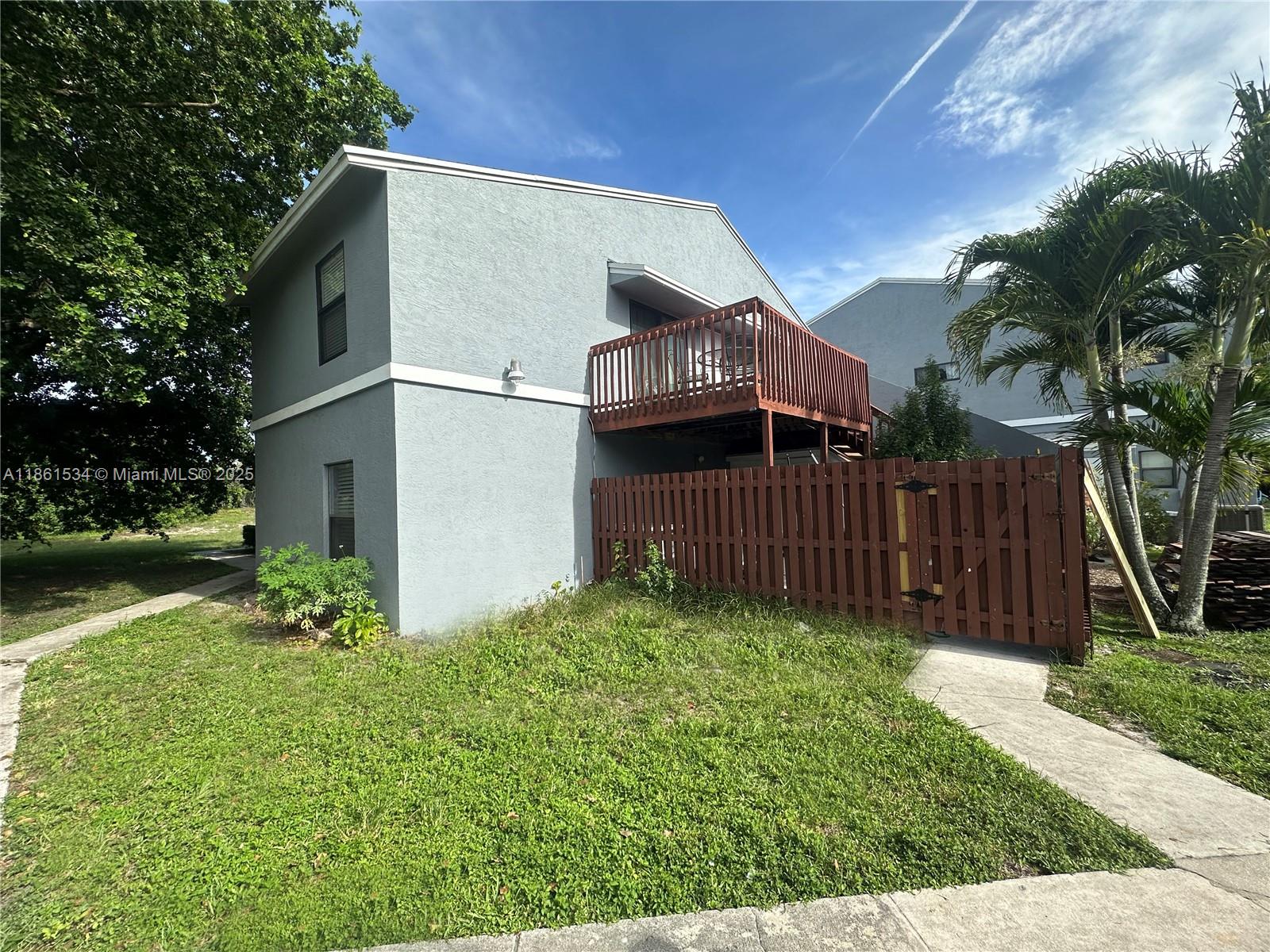 A two-story gray building features a wooden balcony and a fenced-in yard area — 22 Crossings Cir, Boynton Beach FL 33435, BOYNTON BEACH, FL