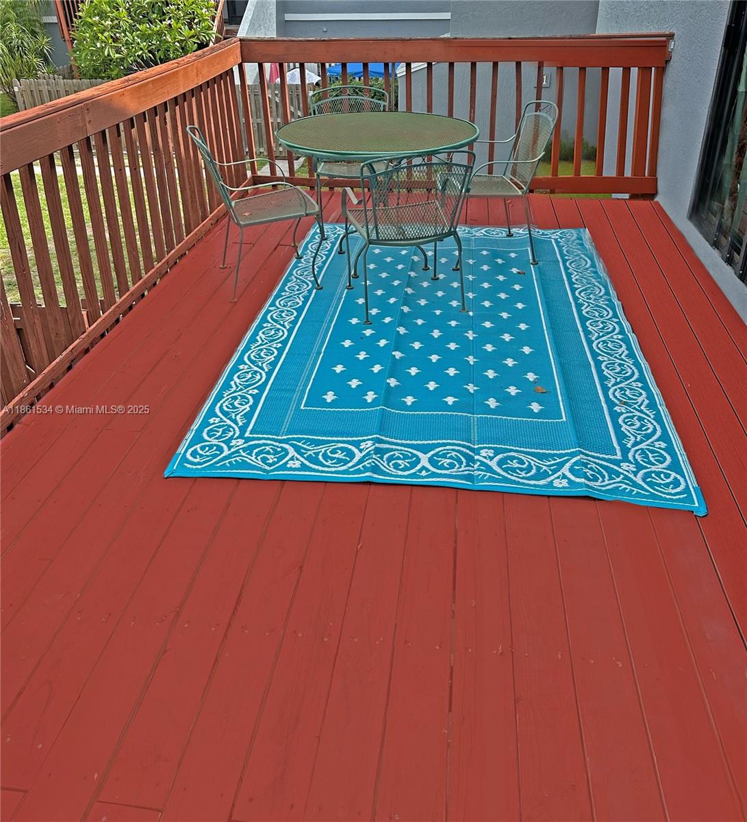 A red wooden deck features a green metal patio set on a blue patterned rug — 22 Crossings Cir, Boynton Beach FL 33435, BOYNTON BEACH, FL