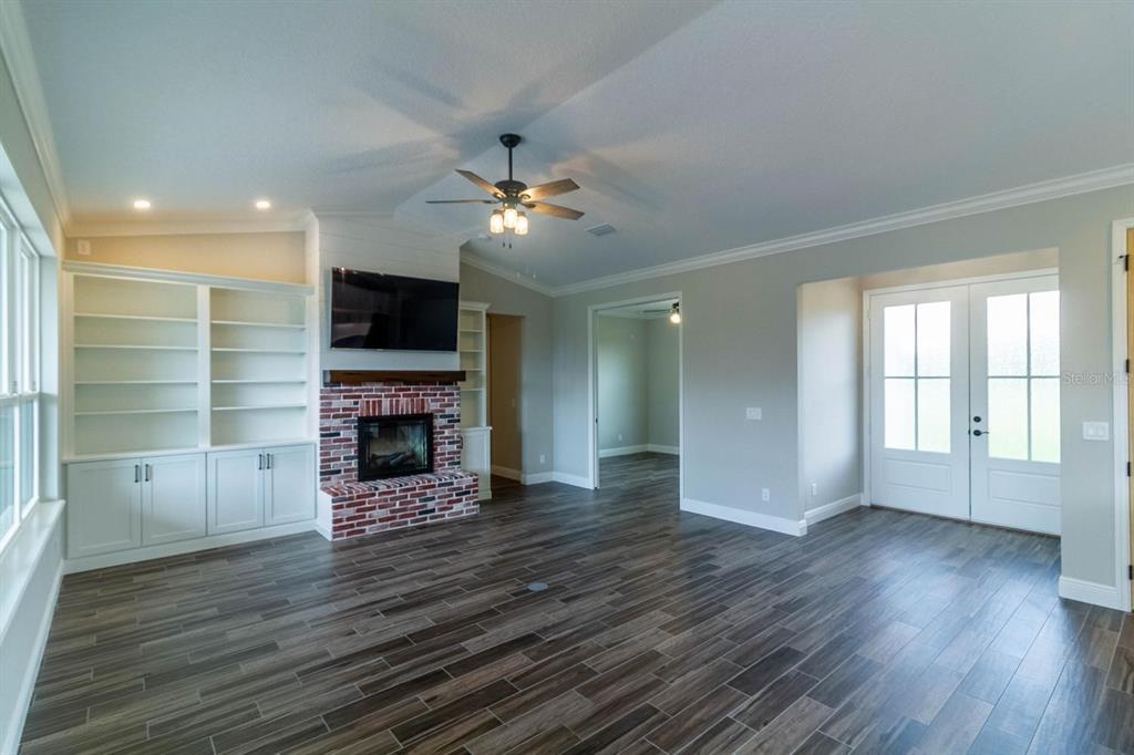 A living room features a brick fireplace, built-in shelving, wood-look tile flooring, and French doors — TBD LOT 1 BENTLEY ROAD, LEESBURG, FL