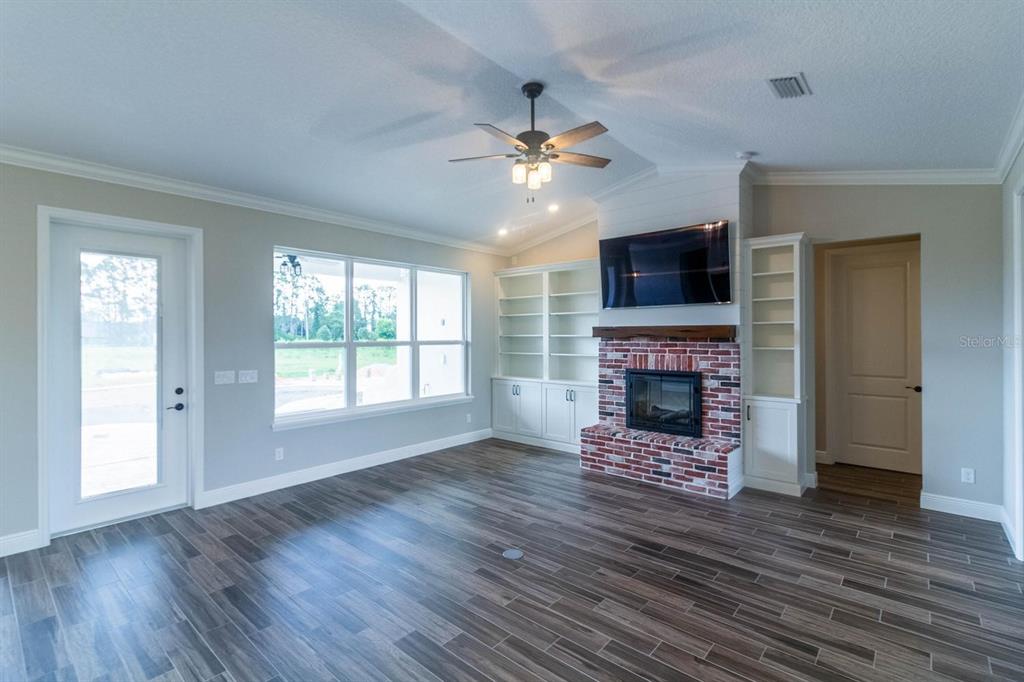 A living room features wood-look tile floors, a brick fireplace, built-in shelving, and a ceiling fan — TBD LOT 1 BENTLEY ROAD, LEESBURG, FL