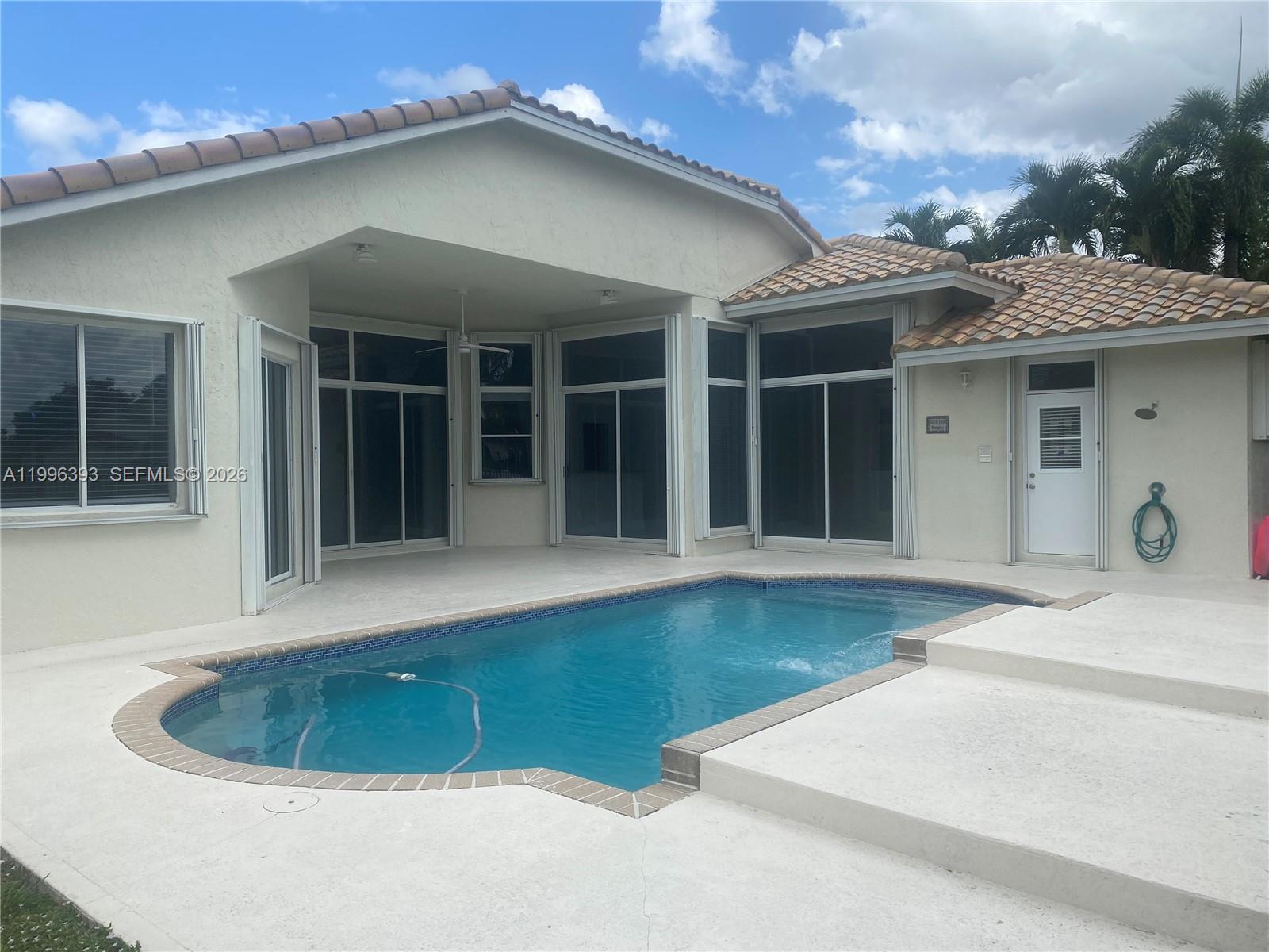 A swimming pool sits on a patio adjacent to a house with a tiled roof — 3066 Lakewood Cir # 3066, Weston FL 33332, WESTON, FL