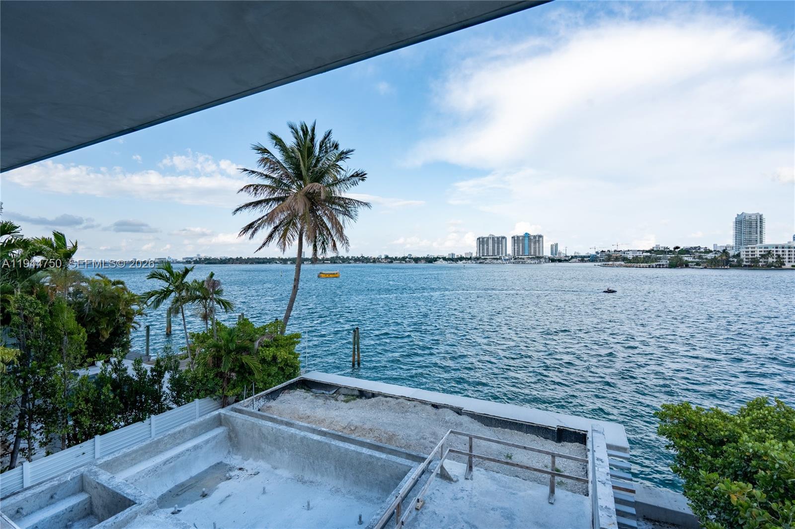 An unfinished concrete pool deck overlooks a bay with palm trees and distant city buildings — 333 E Rivo Alto Dr, Miami Beach FL 33139, MIAMI BEACH, FL