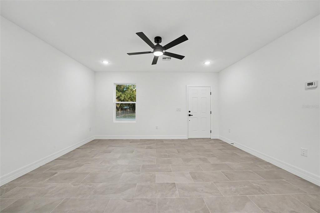 A bright, empty room features white walls, gray tile flooring, and a black ceiling fan — 2922 W PERRY ROAD, AVON PARK, FL