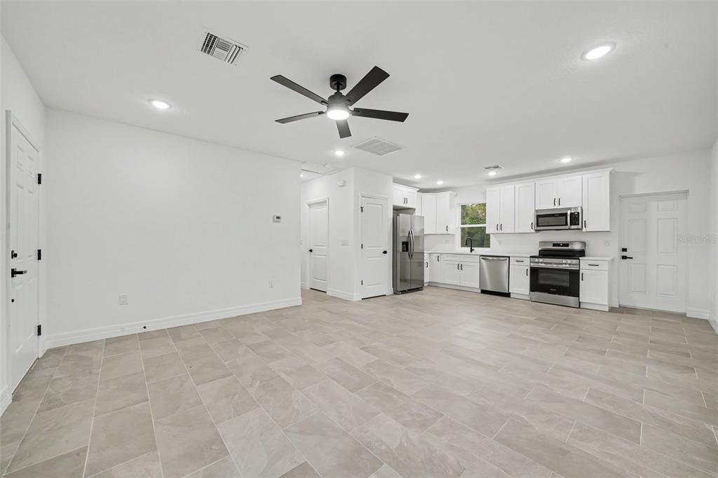 A bright, open-concept kitchen and living area features white cabinetry, stainless appliances, and tile flooring — 2922 W PERRY ROAD, AVON PARK, FL