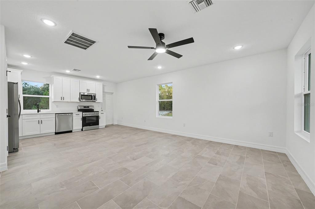 A bright, open-concept kitchen and living area features white cabinetry, stainless appliances, and tile flooring — 2922 W PERRY ROAD, AVON PARK, FL
