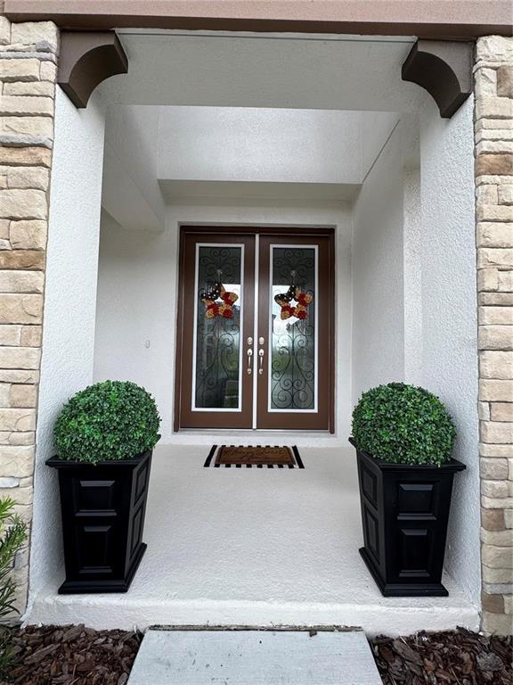 A front entryway features double doors with glass inserts, two potted topiaries, and stone siding — 13150 WELLSPRING DRIVE, LITHIA, FL