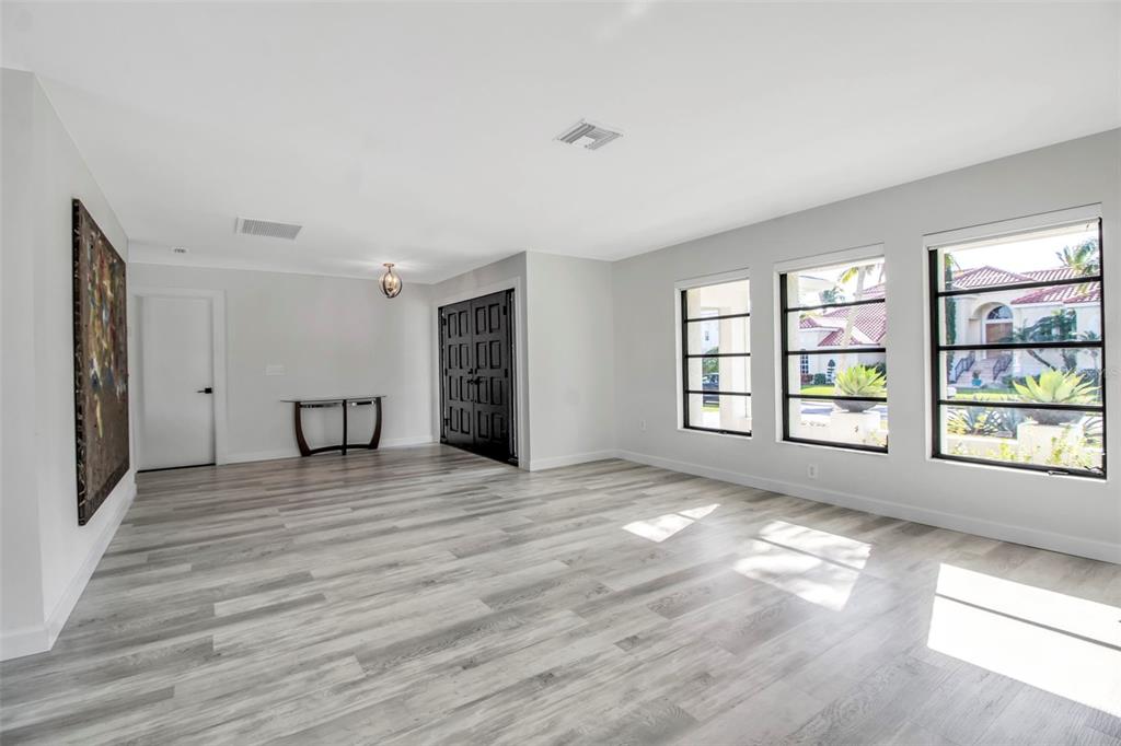 A bright, empty room features light wood-look flooring, white walls, and large windows — 1649 STANFORD LANE, SARASOTA, FL