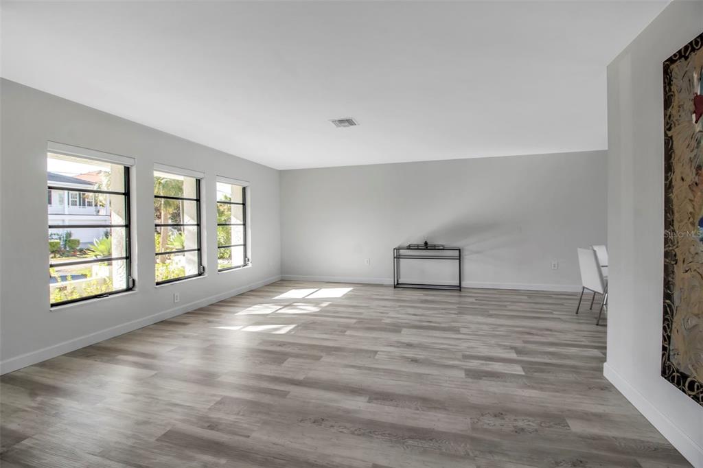 A bright, unfurnished room features light wood-look flooring, three large windows, and a metal console table — 1649 STANFORD LANE, SARASOTA, FL