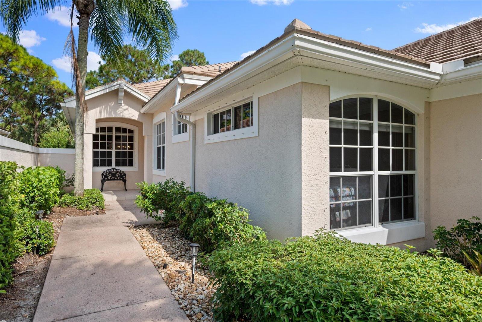 A concrete walkway leads to the entrance of a beige stucco house with arched windows — 3498 SE Doubleton Drive, Stuart FL 34997, STUART, FL