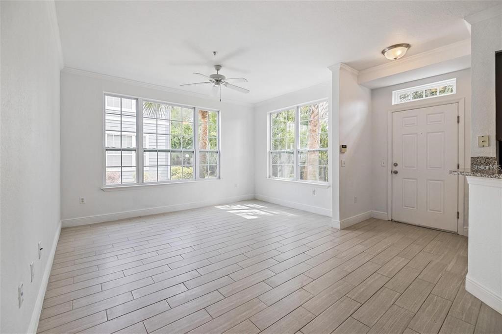 An empty room with white walls, light wood-look tile flooring, large windows, and a ceiling fan — 5571 ROSEHILL ROAD UNIT 104, SARASOTA, FL