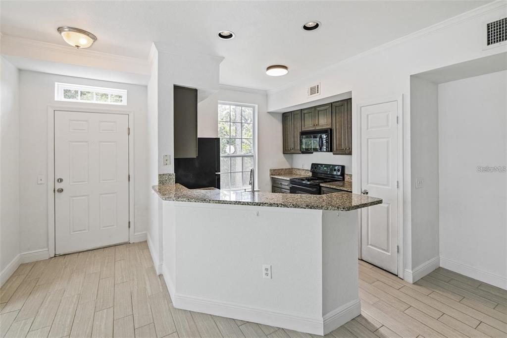 A kitchen features granite countertops, dark wood cabinets, and light-colored tile flooring — 5571 ROSEHILL ROAD UNIT 104, SARASOTA, FL