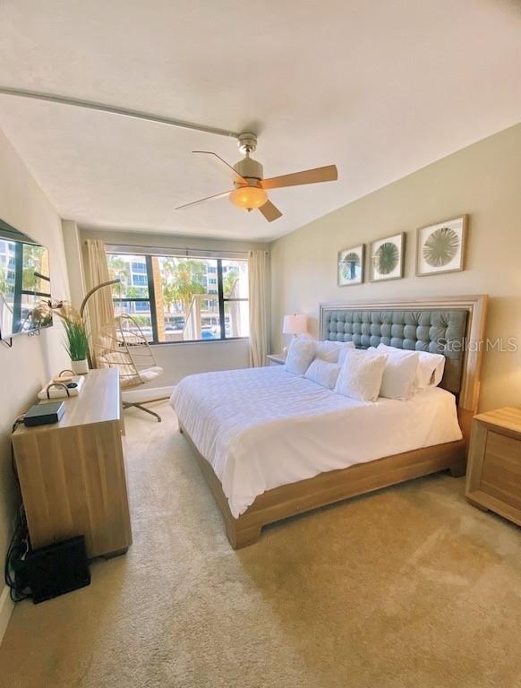 A bedroom features a tufted headboard, a ceiling fan, and a large window with blinds — 5855 MIDNIGHT PASS ROAD UNIT 108, SARASOTA, FL