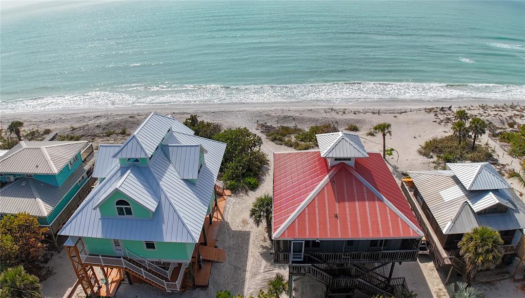 An aerial view shows three elevated beach houses with metal roofs along a sandy coastline — 8796 GRAND AVENUE, PLACIDA, FL