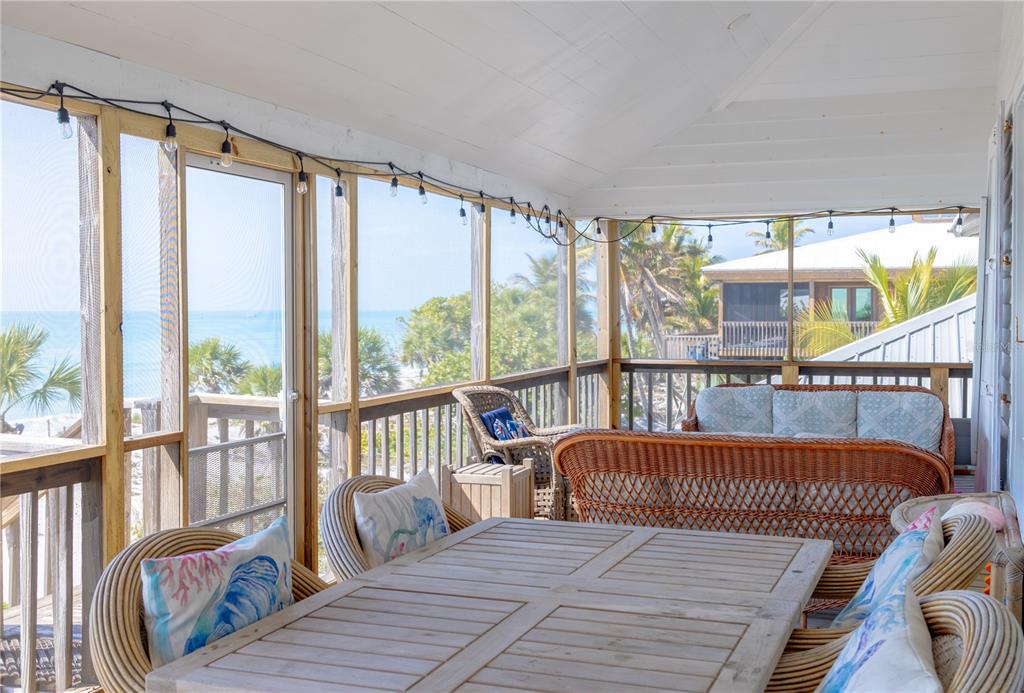 A screened-in porch features wicker furniture, a wooden dining table, and views of the ocean — 8796 GRAND AVENUE, PLACIDA, FL