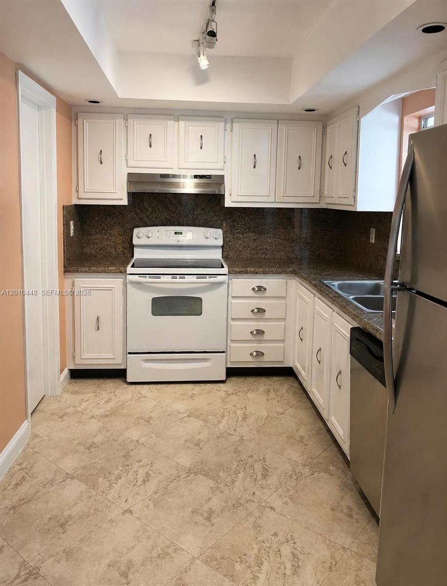 A kitchen features white cabinets, granite countertops, a white stove, and a stainless steel refrigerator — 1601 N K St, Lake Worth FL 33460, LAKE WORTH, FL