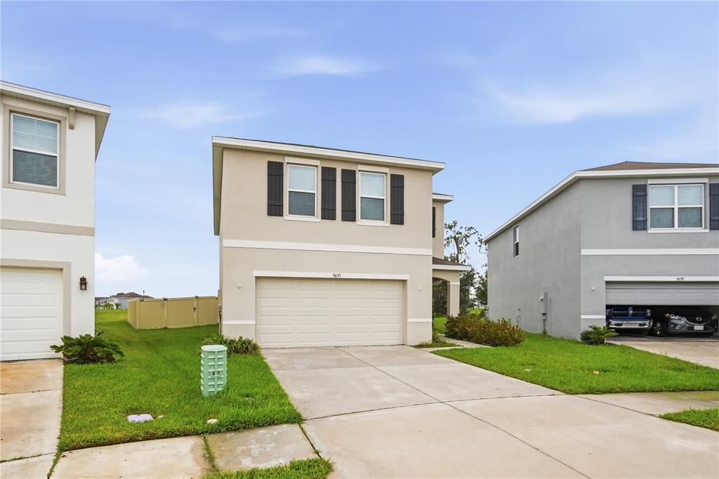 A two-story suburban house with a beige exterior, a two-car garage, and a concrete driveway — 5635 HOLLINGWORTH TRAIL, WESLEY CHAPEL, FL