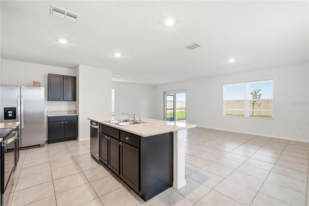 A kitchen with dark cabinets, a granite-topped island, and tile flooring opens to a living area — 5635 HOLLINGWORTH TRAIL, WESLEY CHAPEL, FL
