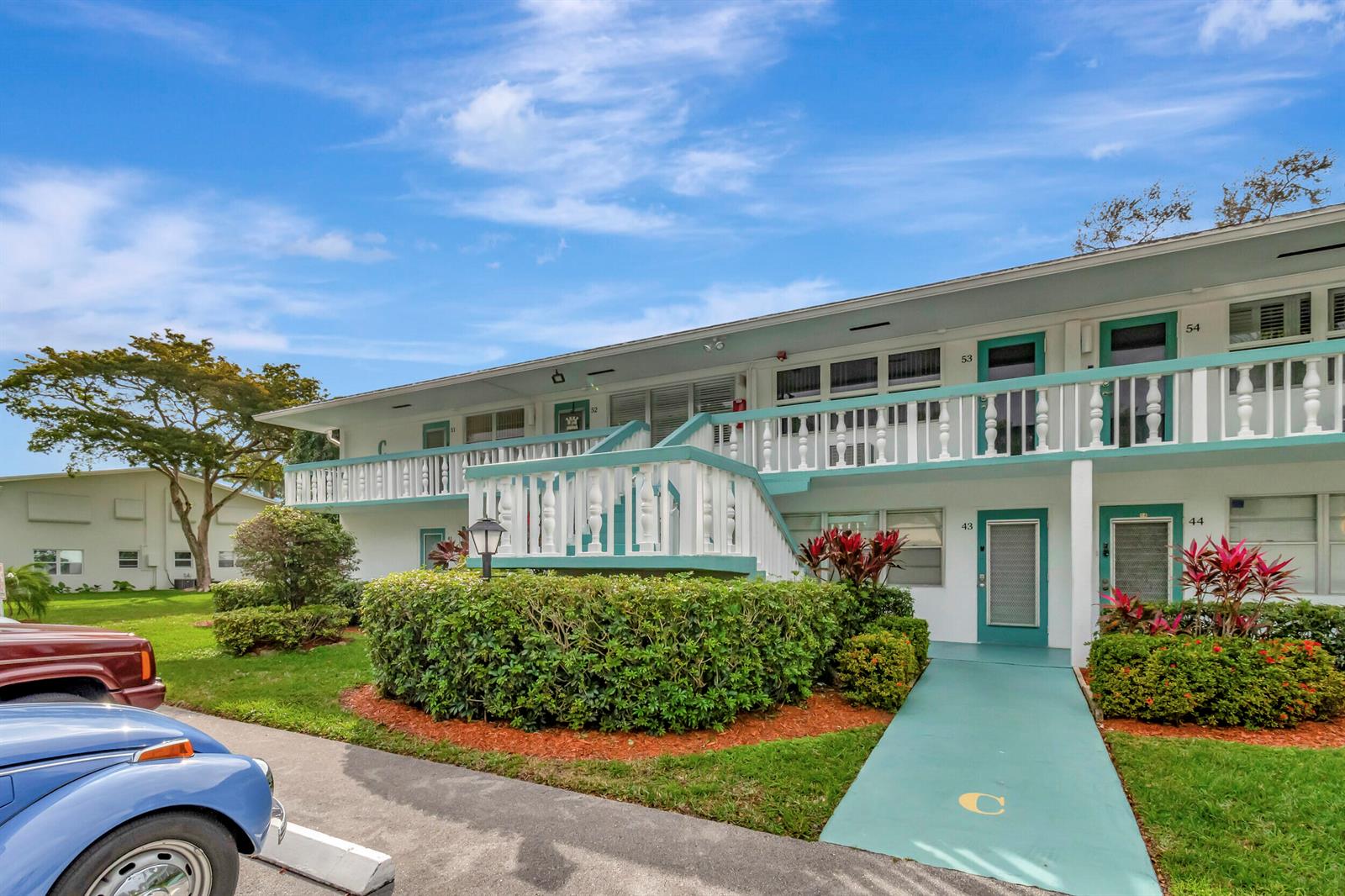 A two-story apartment building features white exterior walls, teal trim, and a central staircase — 51 Ventnor C, Deerfield Beach FL 33442, DEERFIELD BEACH, FL