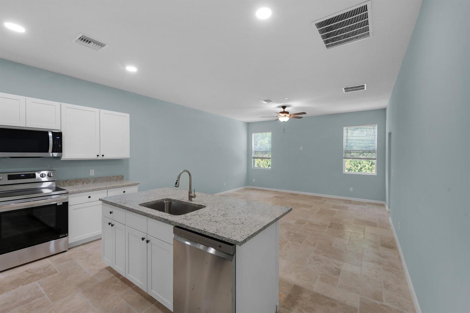 A kitchen with white cabinets, granite countertops, and a center island opens to a living area — VERO BEACH, FL