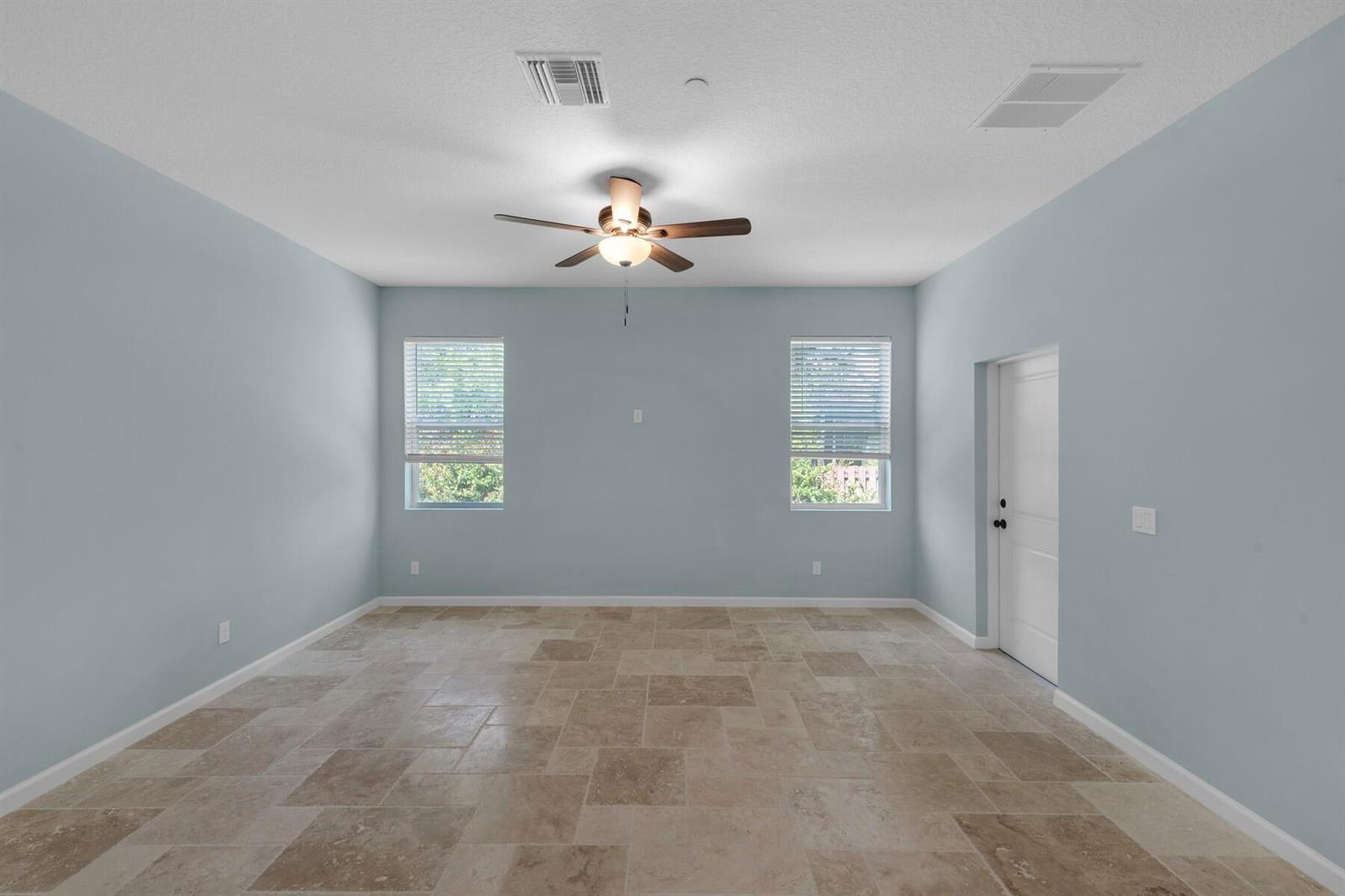 An empty room with light blue walls, tile flooring, two windows, and a ceiling fan — VERO BEACH, FL