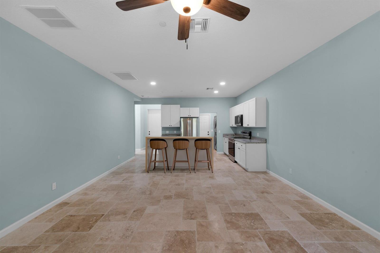 A kitchen with white cabinets, a central island with three stools, and light-colored tile flooring — VERO BEACH, FL