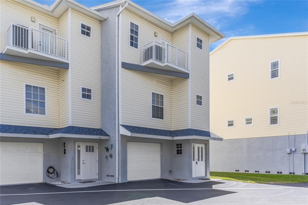 The exterior of a multi-story townhouse with light yellow siding, gray stucco, and two garages — 19803 GULF BOULEVARD UNIT 301, INDIAN SHORES, FL