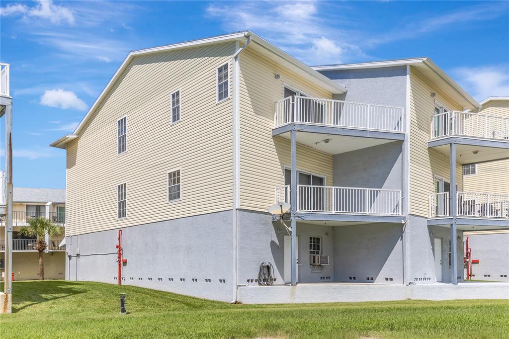 The exterior of a multi-story building featuring yellow siding, gray stucco, and stacked balconies — 19803 GULF BOULEVARD UNIT 301, INDIAN SHORES, FL