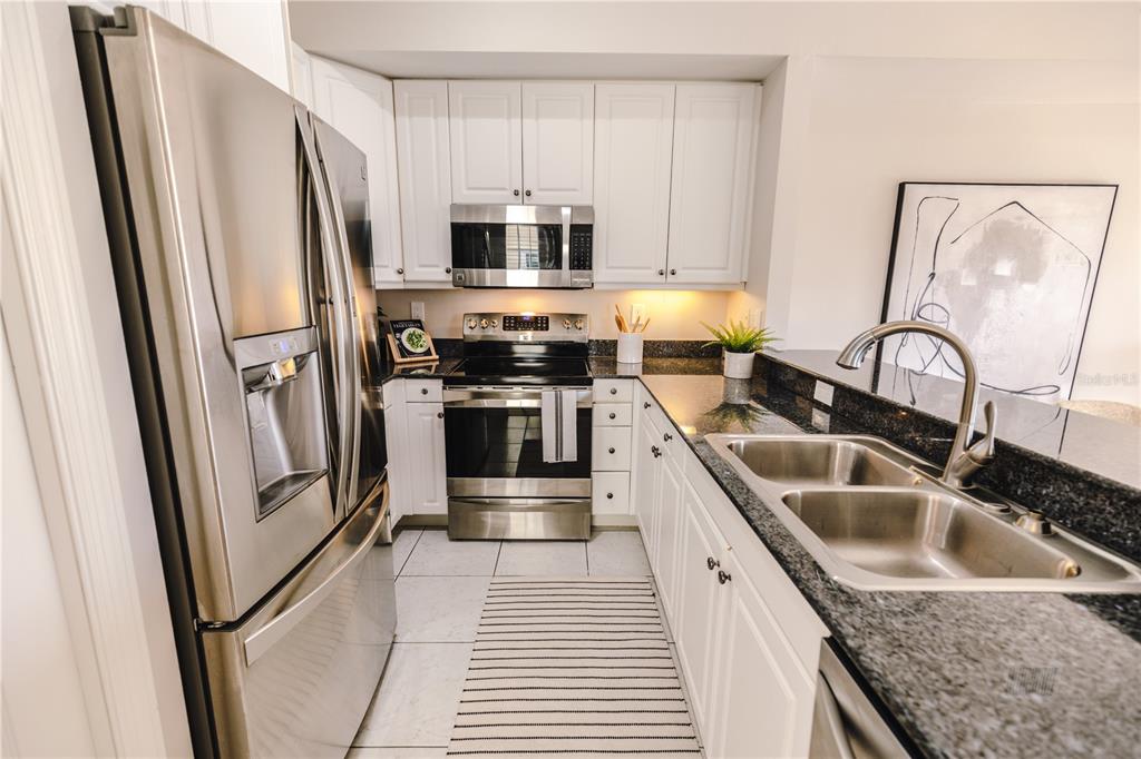 A kitchen features white cabinets, stainless steel appliances, dark granite countertops, and tile flooring — 19803 GULF BOULEVARD UNIT 301, INDIAN SHORES, FL