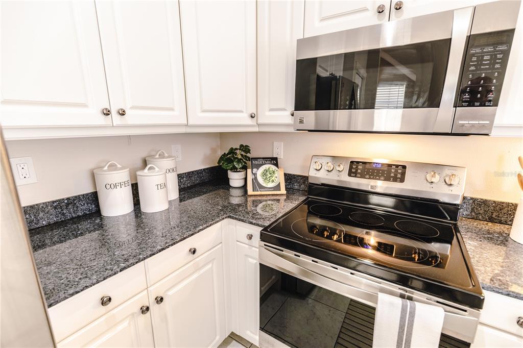 A kitchen features white cabinets, granite countertops, a stainless steel microwave, and an electric stove — 19803 GULF BOULEVARD UNIT 301, INDIAN SHORES, FL
