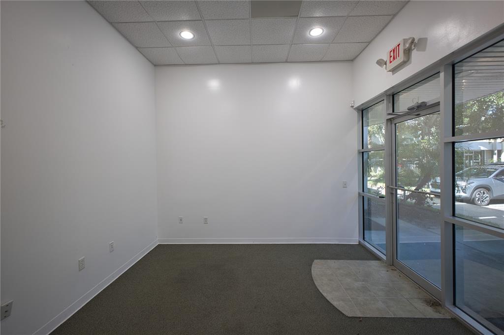 An empty office space features white walls, gray carpeting, recessed ceiling lights, and glass doors — 8810 COMMODITY CIRCLE UNIT 12, ORLANDO, FL