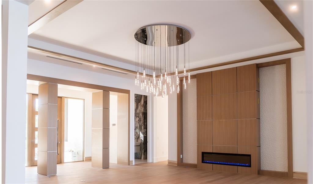 A modern living room features a large tiered chandelier, wood paneling, and a linear fireplace — 1290 HIDDEN HARBOR WAY, SARASOTA, FL