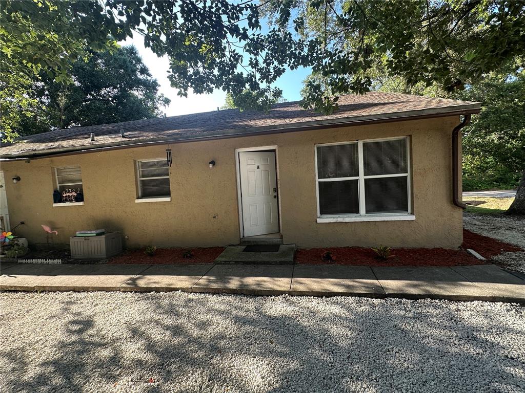 A tan house with a white gable and a cracked concrete driveway under large trees — 9406 N HARTTS DRIVE, TAMPA, FL