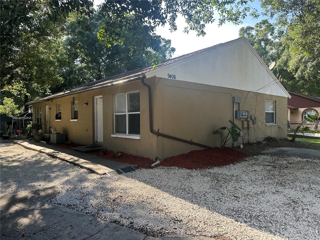 A tan, single-story house with a gravel driveway and a large tree in the yard — 9406 N HARTTS DRIVE, TAMPA, FL