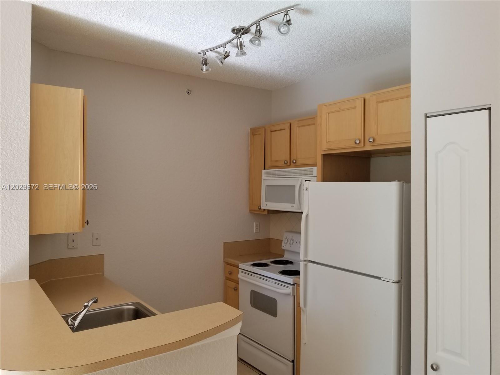 A kitchen features light wood cabinets, white appliances, a stainless steel sink, and track lighting — 6001 SW 70th St # 538, South Miami FL 33143, SOUTH MIAMI, FL