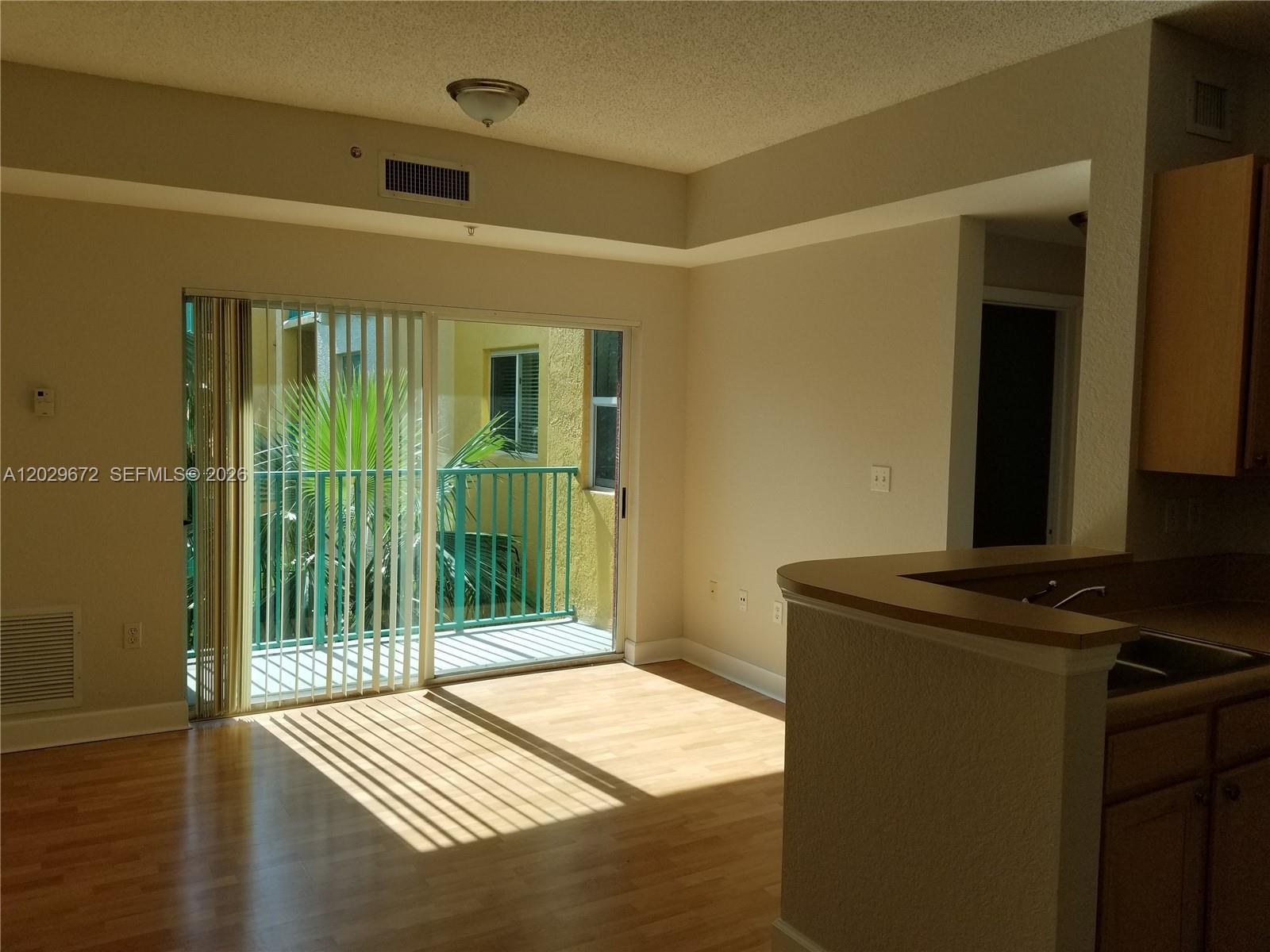 An empty room with light wood flooring, a sliding glass door, and a kitchen counter — 6001 SW 70th St # 538, South Miami FL 33143, SOUTH MIAMI, FL