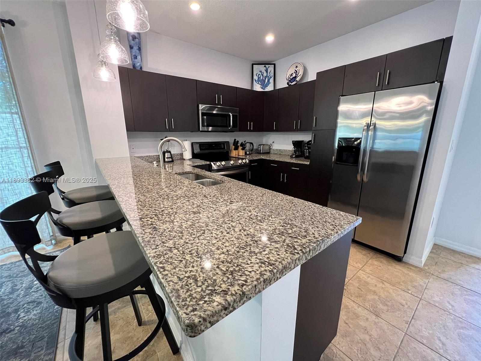 A kitchen features dark wood cabinets, granite countertops, stainless steel appliances, and three bar stools — 2361 SE 5th St, Pompano Beach FL 33062, POMPANO BEACH, FL