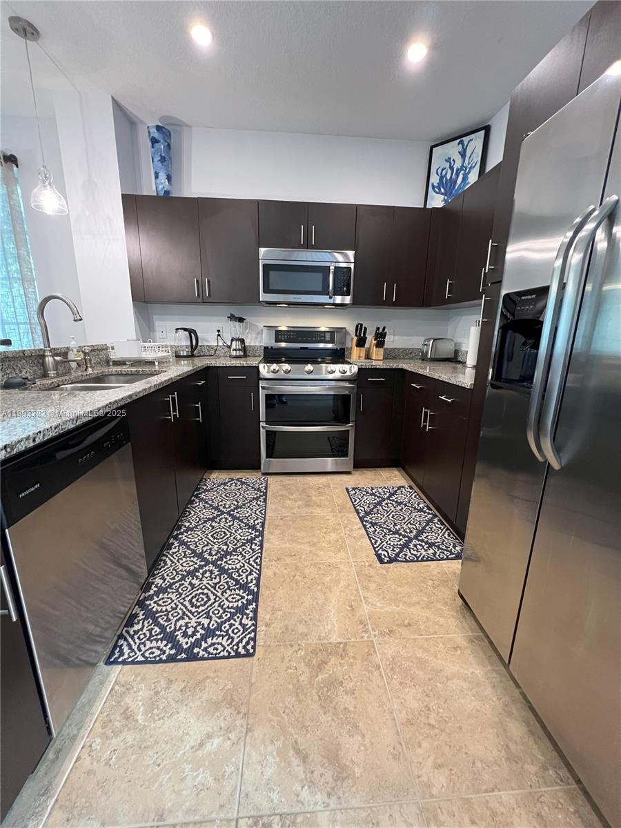 A kitchen features dark wood cabinets, stainless steel appliances, granite countertops, and tile flooring — 2361 SE 5th St, Pompano Beach FL 33062, POMPANO BEACH, FL