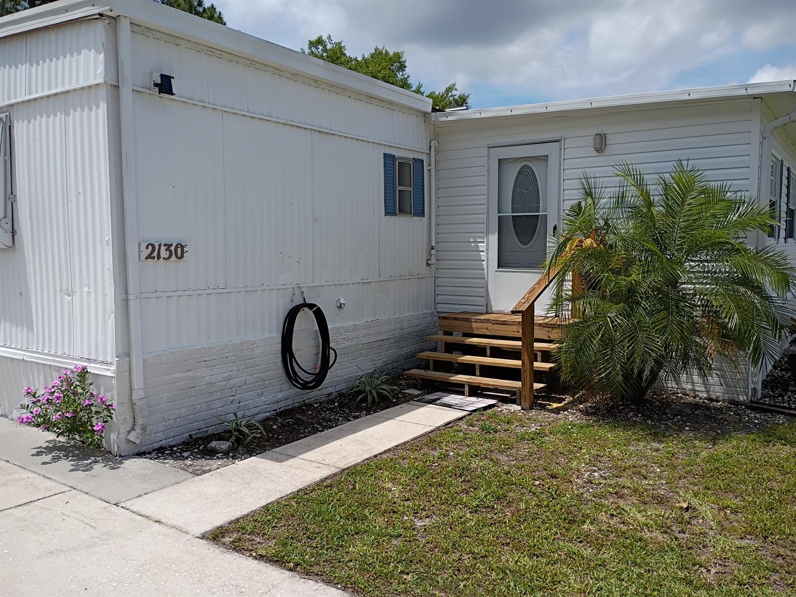 The exterior of a white mobile home features a wooden staircase leading to the front door — 2130 SE 24th Boulevard, Okeechobee FL 34974, OKEECHOBEE, FL