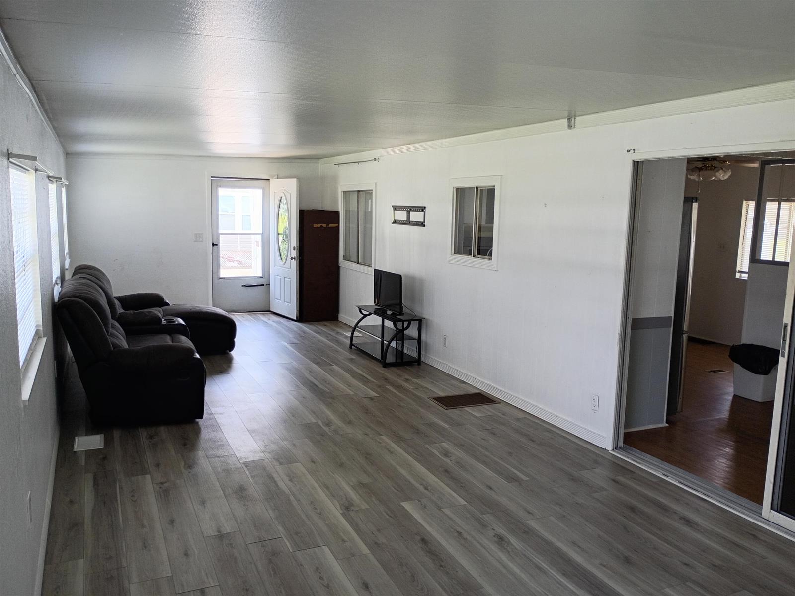 A living room with white walls, wood-look flooring, a dark recliner, and a television stand — 2130 SE 24th Boulevard, Okeechobee FL 34974, OKEECHOBEE, FL