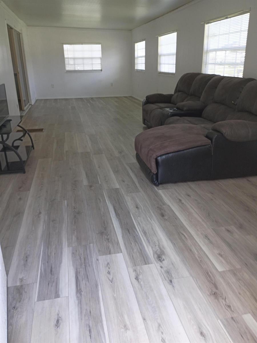 A living room with light wood-look flooring, white walls, and a brown reclining sofa — 2130 SE 24th Boulevard, Okeechobee FL 34974, OKEECHOBEE, FL