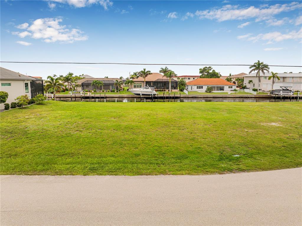 A grassy vacant lot sits along a canal with houses and boats in the background — 5 TROPICANA DRIVE, PUNTA GORDA, FL