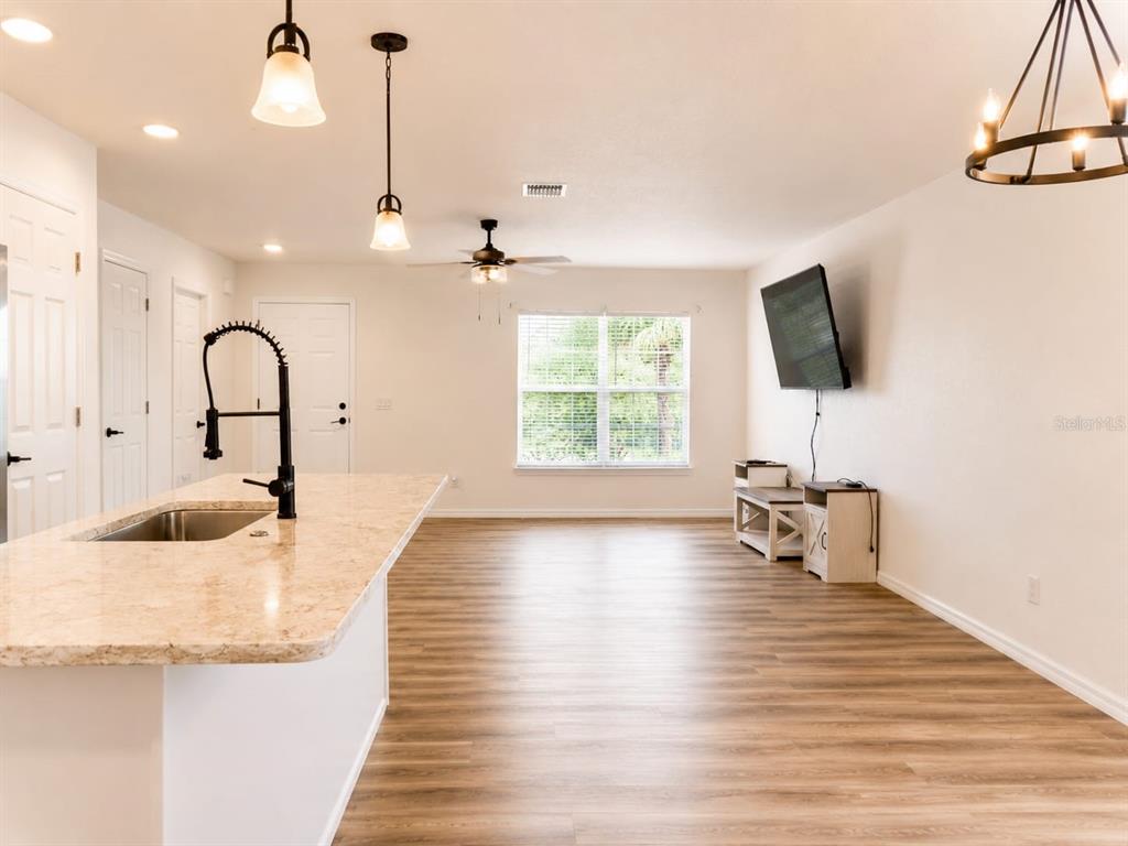 A kitchen island with a sink overlooks an open living area with wood-look flooring — 318 EUCALYPTUS ROAD, LAKE WALES, FL