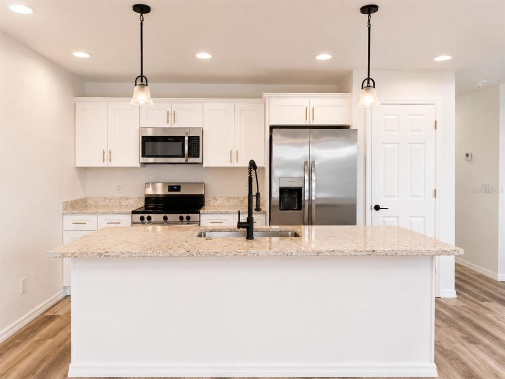 A kitchen features white cabinets, stainless steel appliances, a granite island, and wood-look flooring — 318 EUCALYPTUS ROAD, LAKE WALES, FL