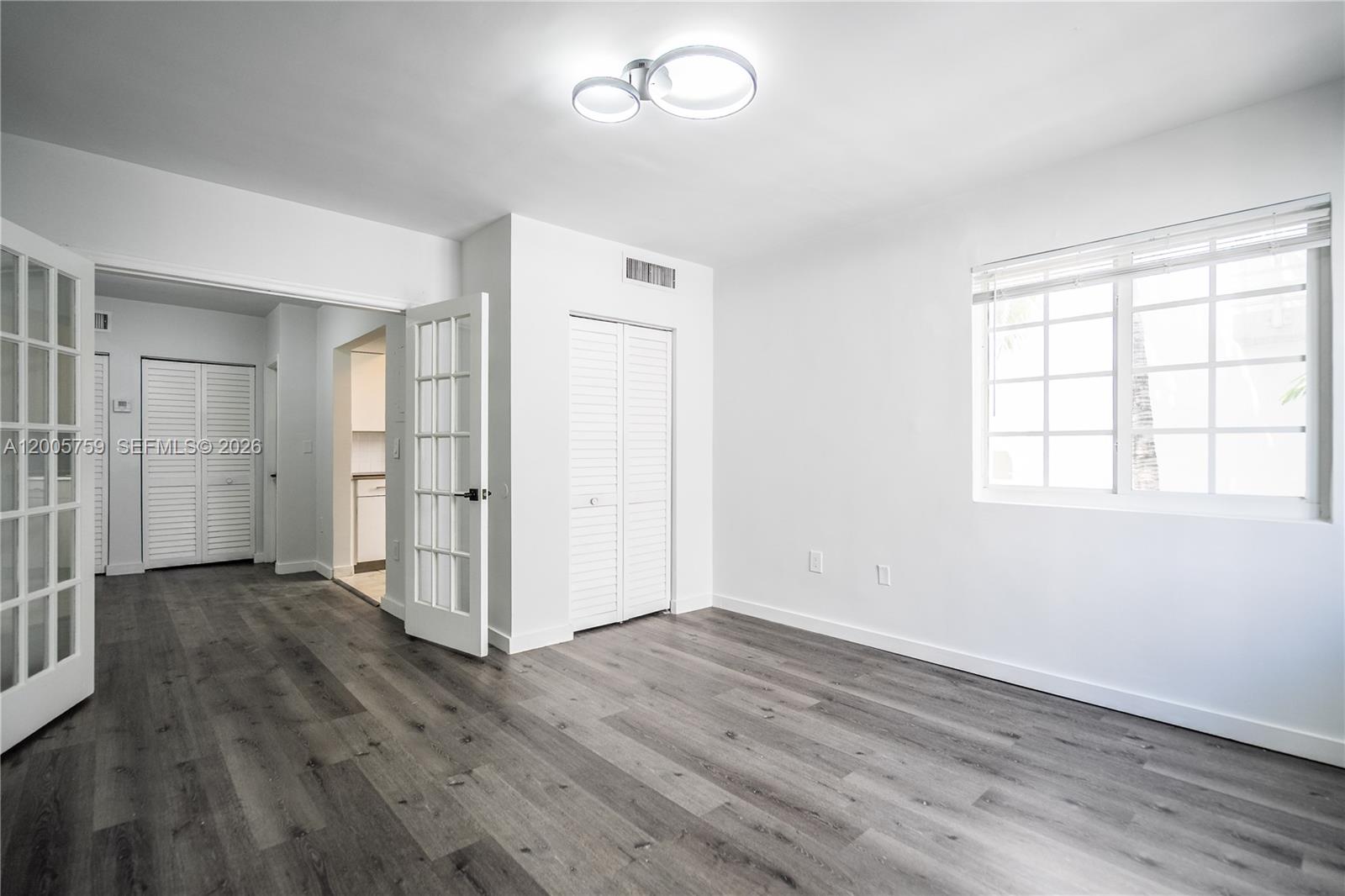 An empty room features white walls, gray wood-look flooring, a window, and French doors — 920 Pennsylvania Ave # 206, Miami Beach FL 33139, MIAMI BEACH, FL