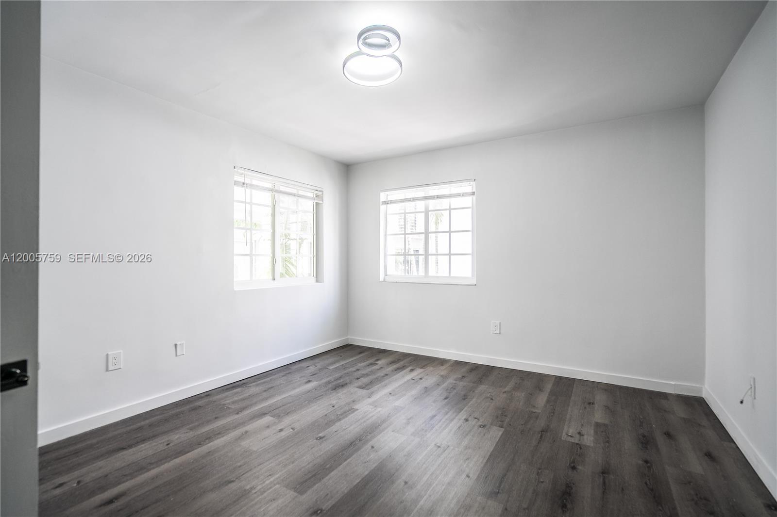 An empty bedroom features white walls, dark wood-look flooring, and two windows — 920 Pennsylvania Ave # 206, Miami Beach FL 33139, MIAMI BEACH, FL